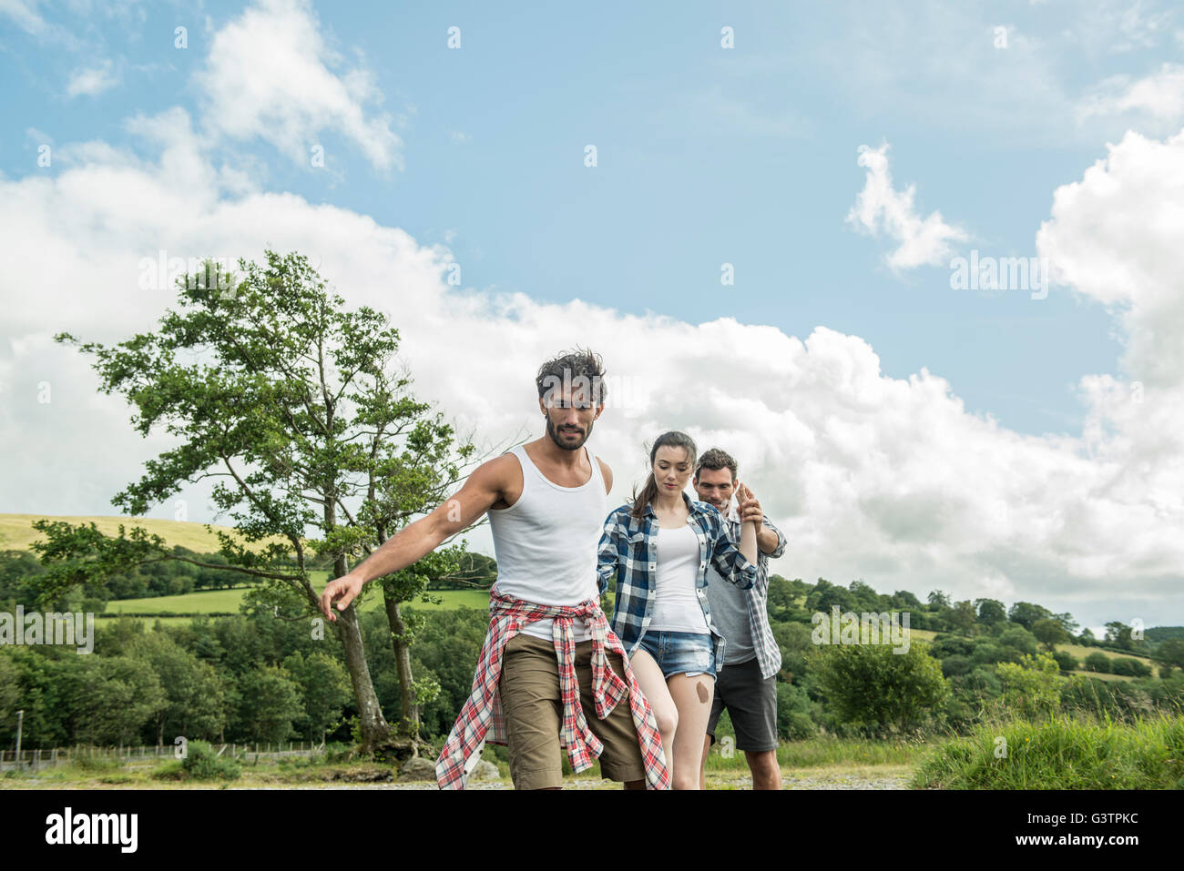 Three friends holding hands crossing a shallow river on the shore of Bala Lake in Wales. Stock Photo