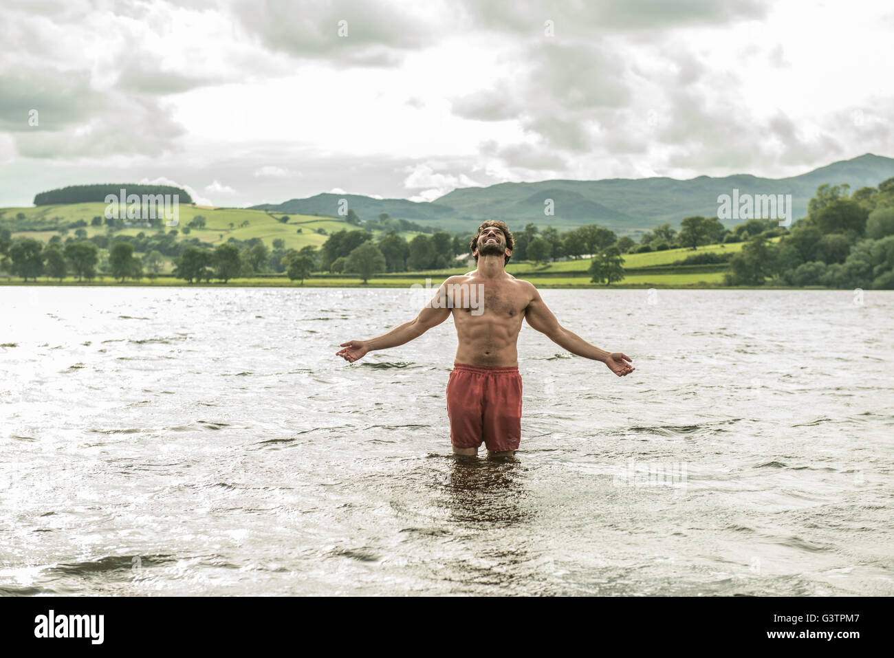A man standing with arms outstretched in the shallow water of Bala Lake ...