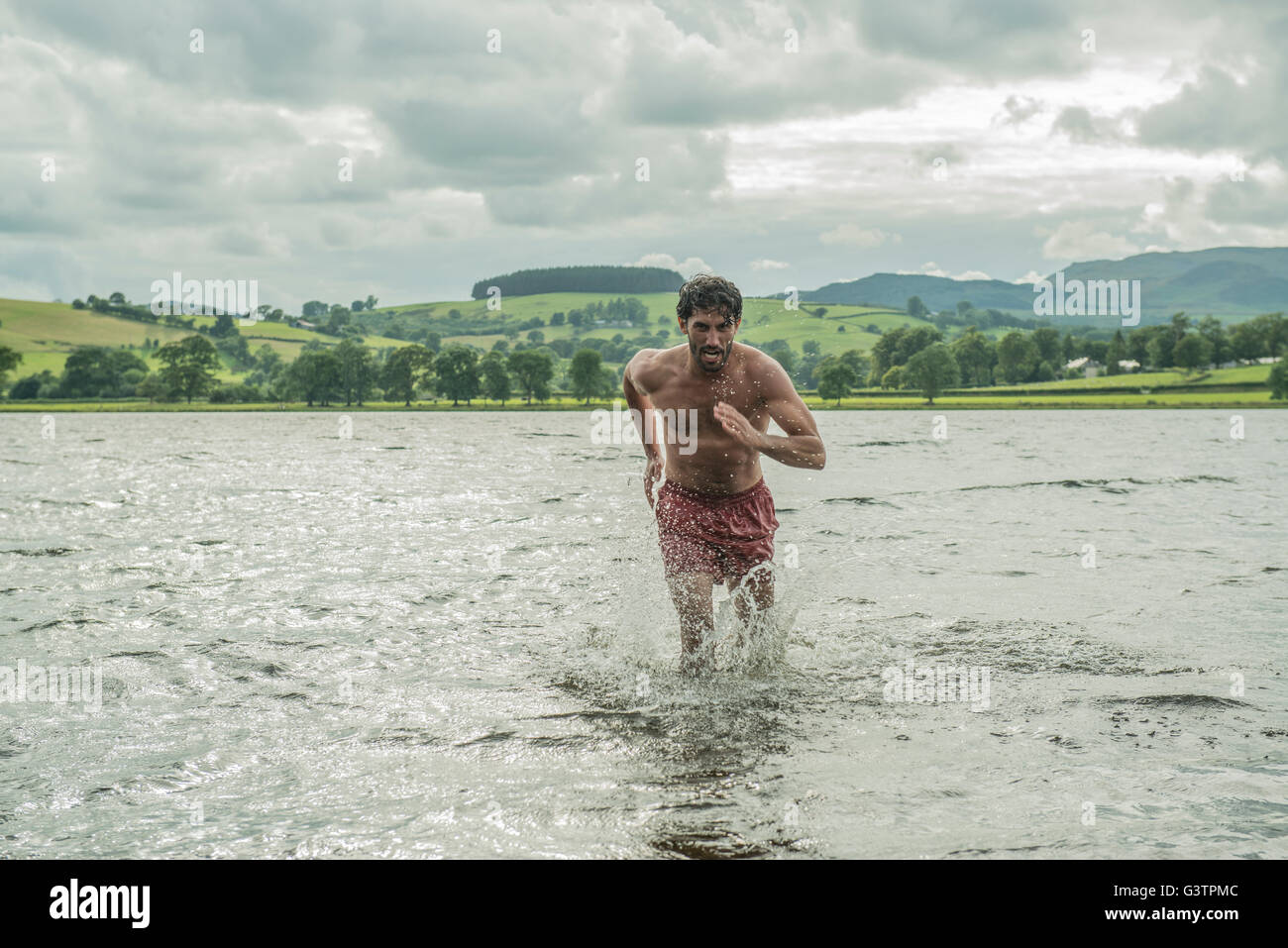 A fit man running through the shallow water of Bala Lake in Wales. Stock Photo