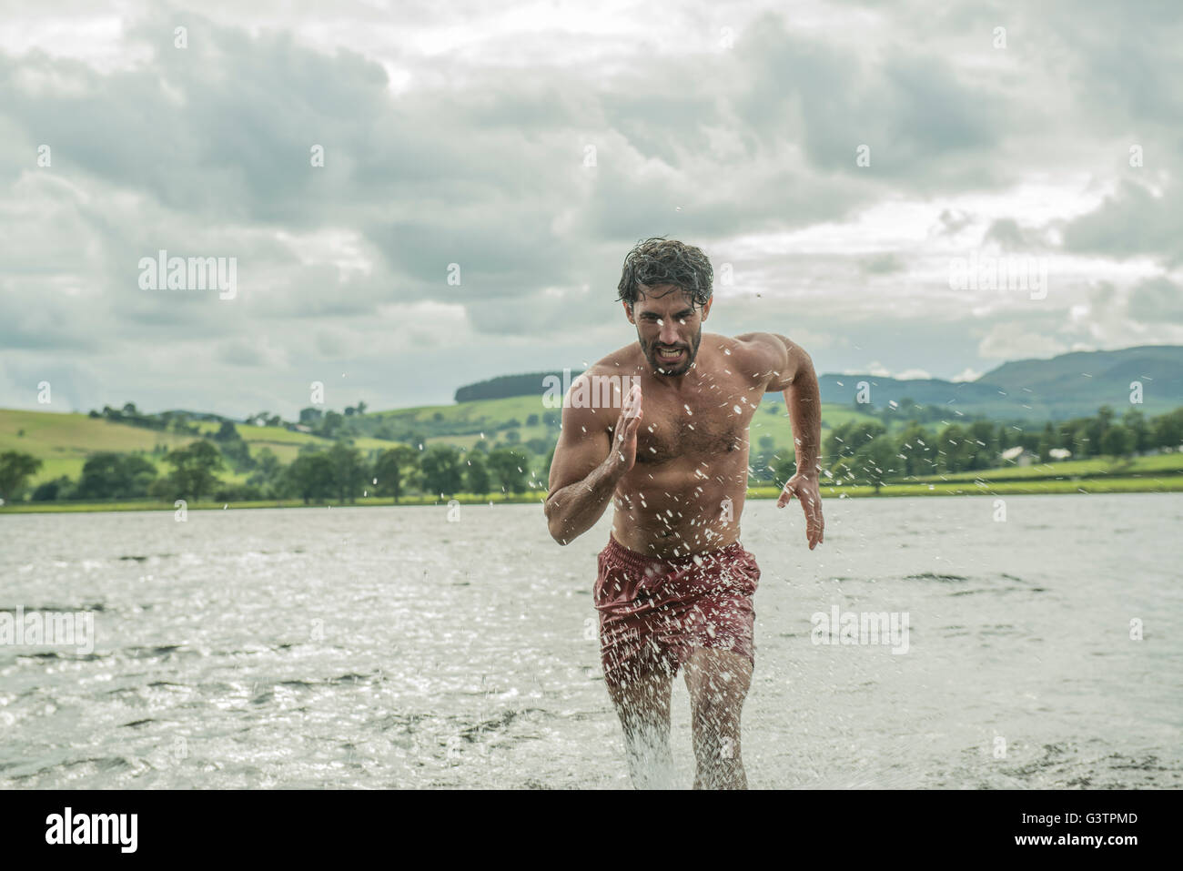 A fit man running through the shallow water of Bala Lake in Wales. Stock Photo