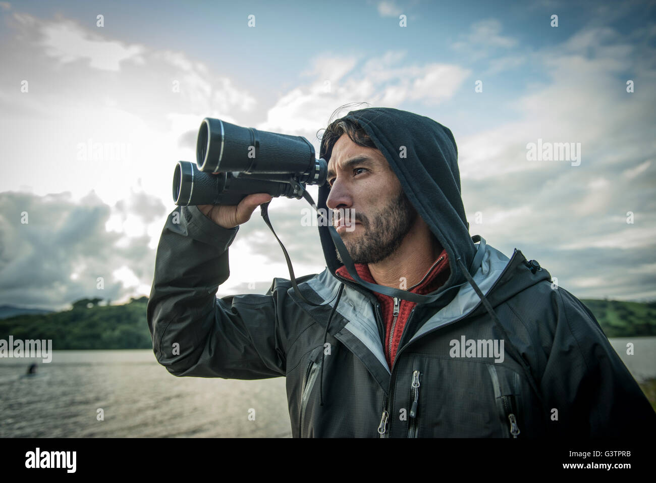 A bearded man in hiking clothes using binoculars on the shore of Bala Lake in Wales. Stock Photo