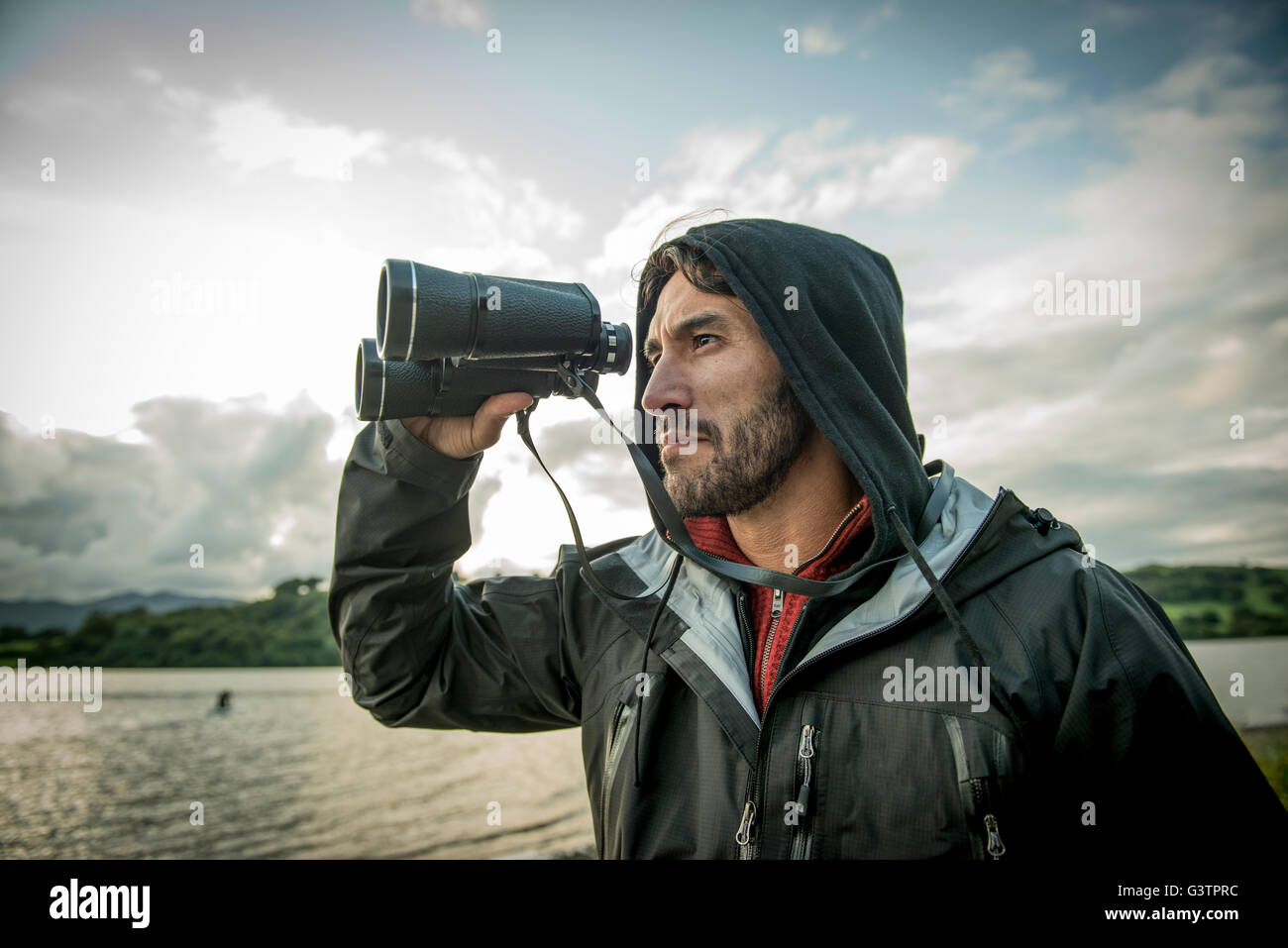 A bearded man in hiking clothes using binoculars on the shore of Bala Lake in Wales. Stock Photo