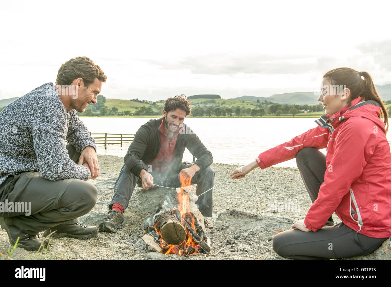 Three friends relax around a campfire on the shore of Bala Lake in Wales. Stock Photo