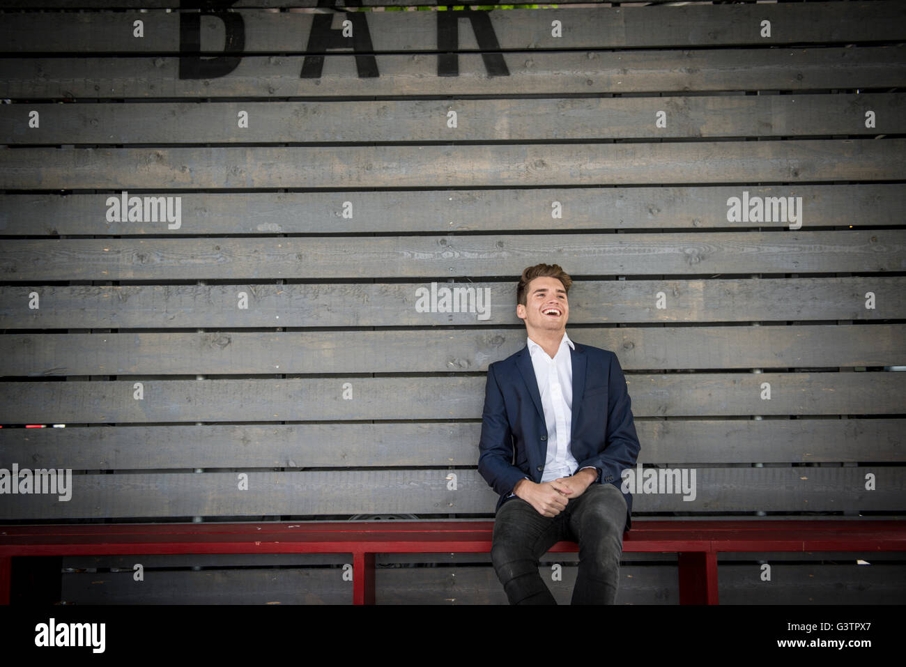 A young man sitting on a bench behind a bar on the South Bank in London. Stock Photo