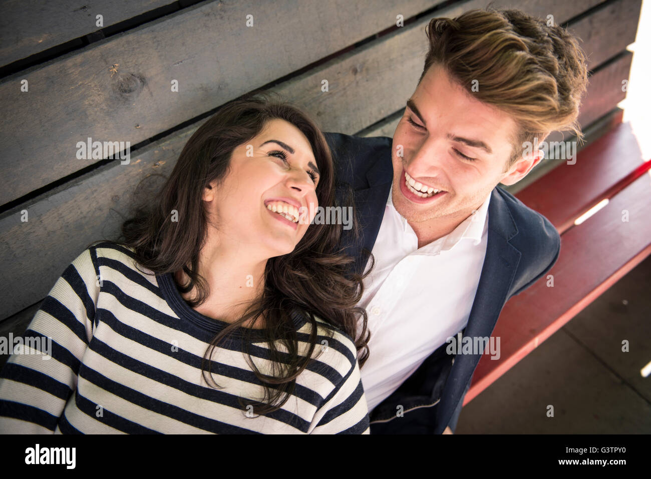 A young couple sitting on a bench behind a bar on the South Bank in London. Stock Photo