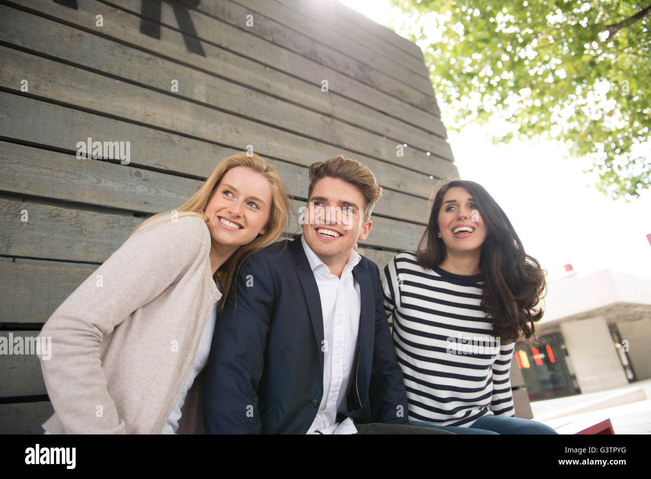 Three friends sitting on a bench on the South Bank in London. Stock Photo