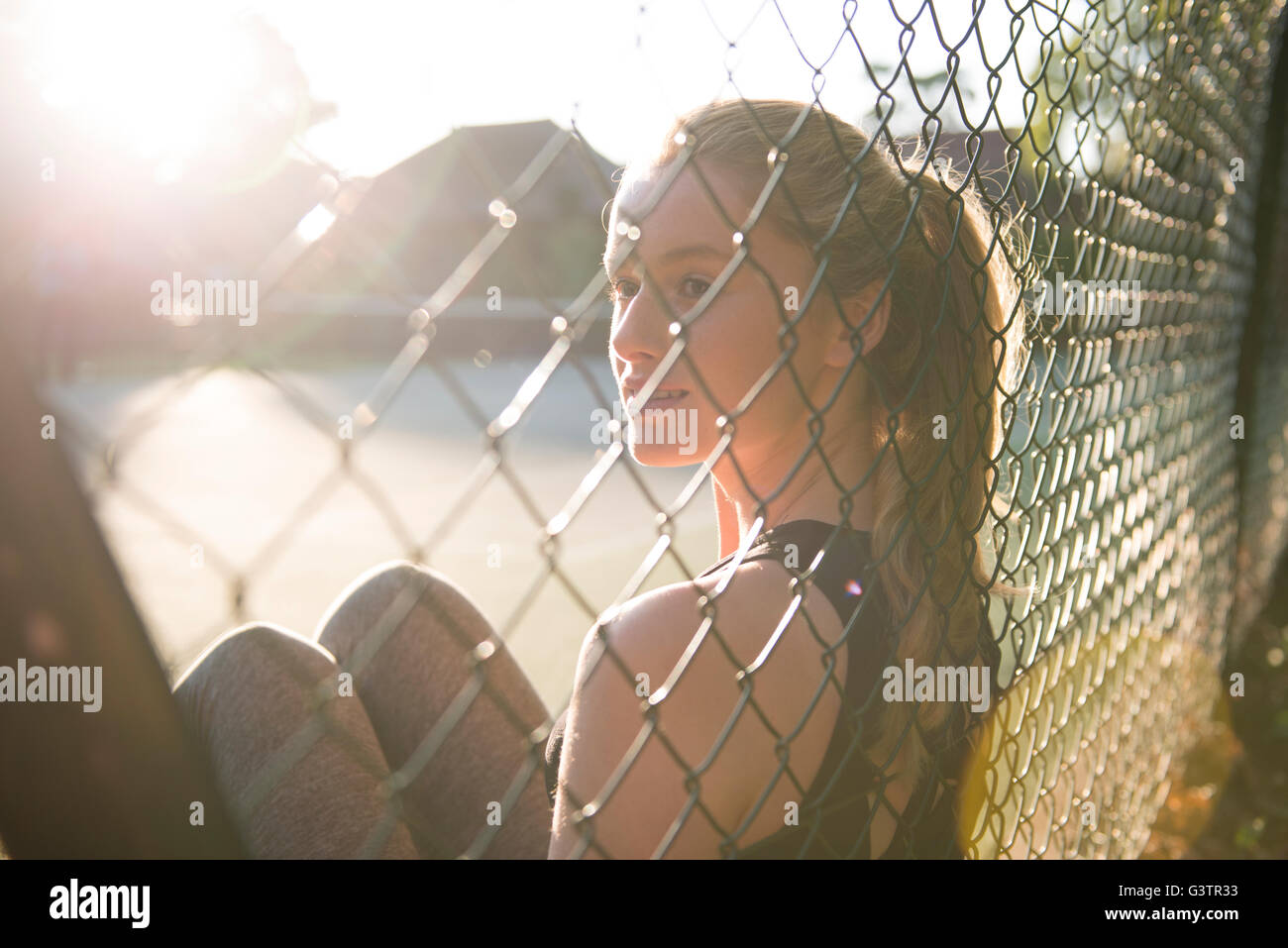 A young woman enjoying the evening sunshine sat on a tennis court. Stock Photo