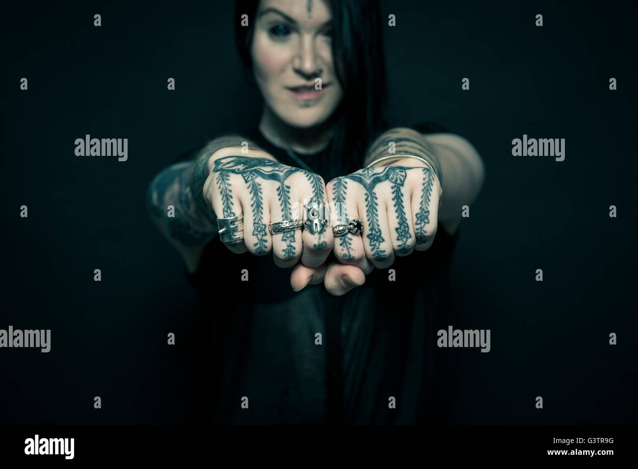 Studio portrait of a young woman with tattooed arms and face. Stock Photo
