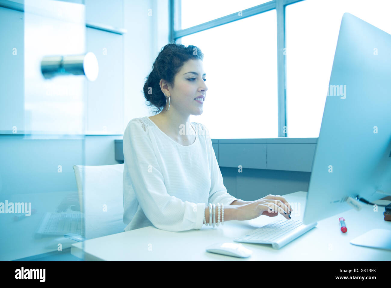A professional woman sitting in front of a computer in an office environment. Stock Photo