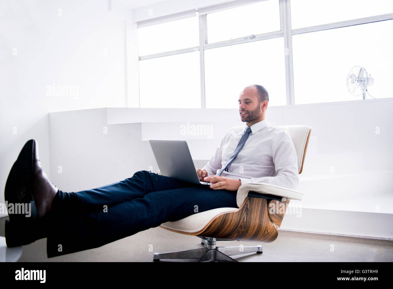 A professional man sitting making notes on a laptop in a business environment. Stock Photo