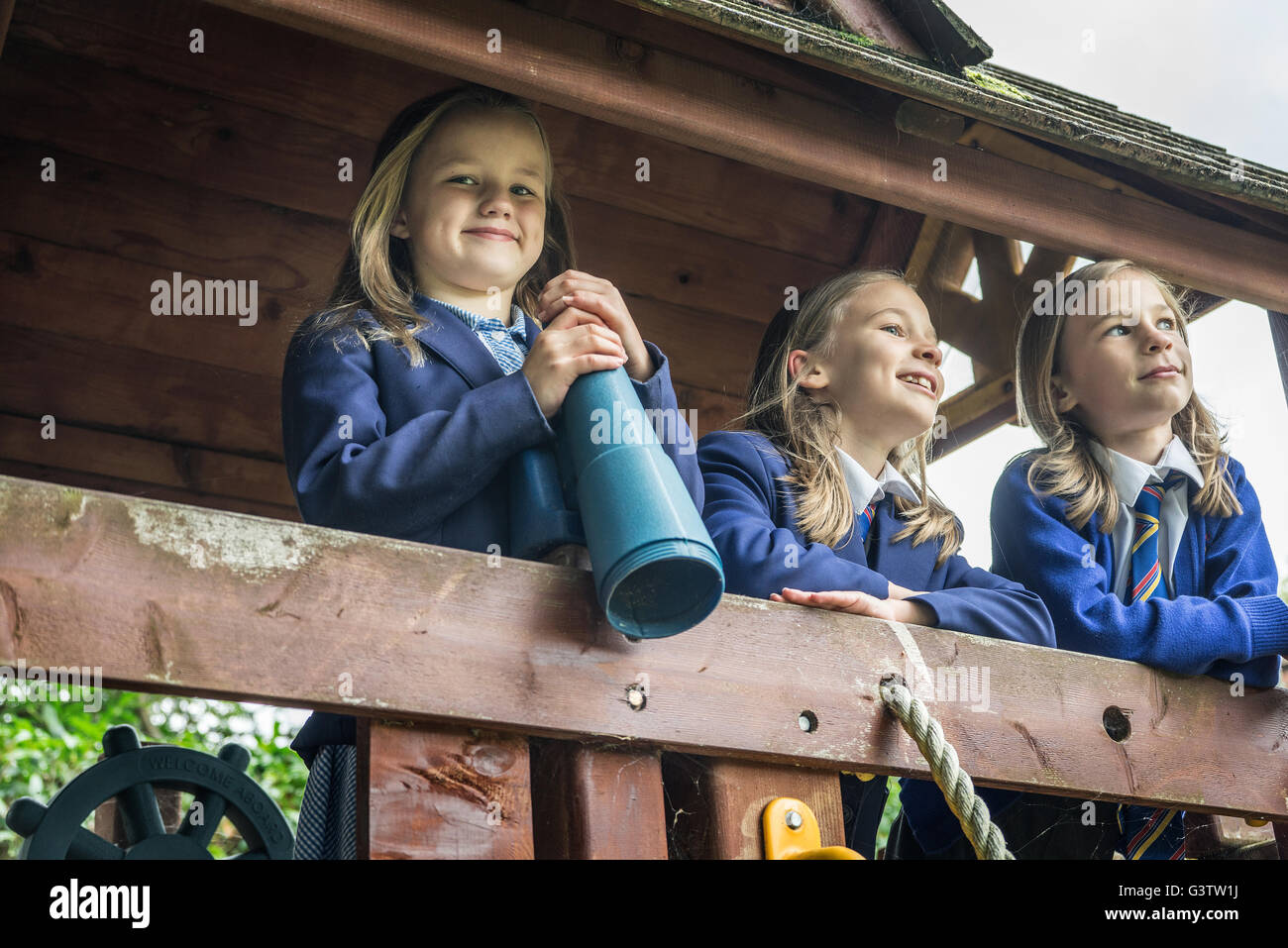 Three girls in school uniform stand together on wooden playground apparatus. Stock Photo