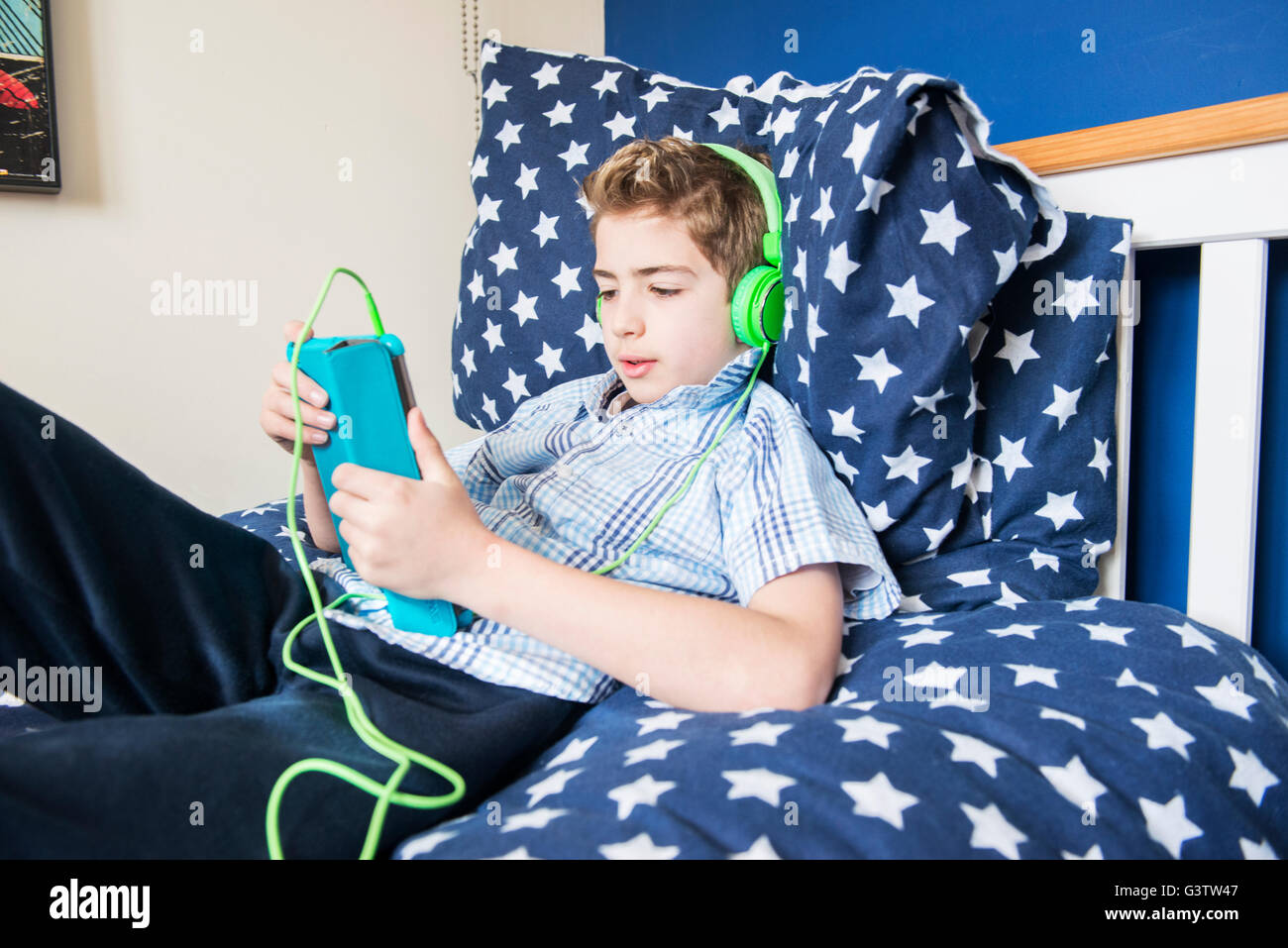 A ten year old boy laying on a bed listening to music on earphones