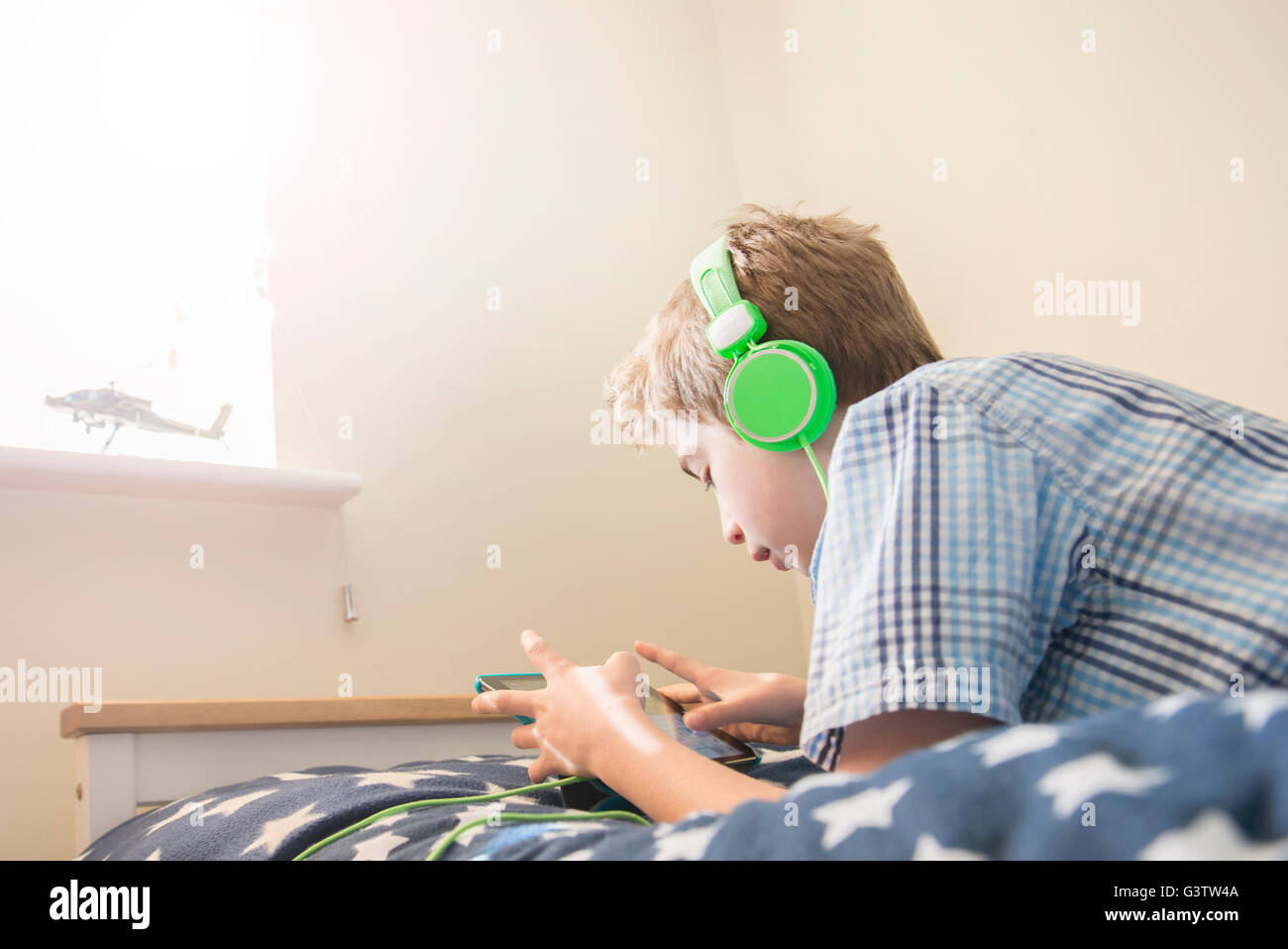 A ten year old boy laying on a bed listening to music on earphones