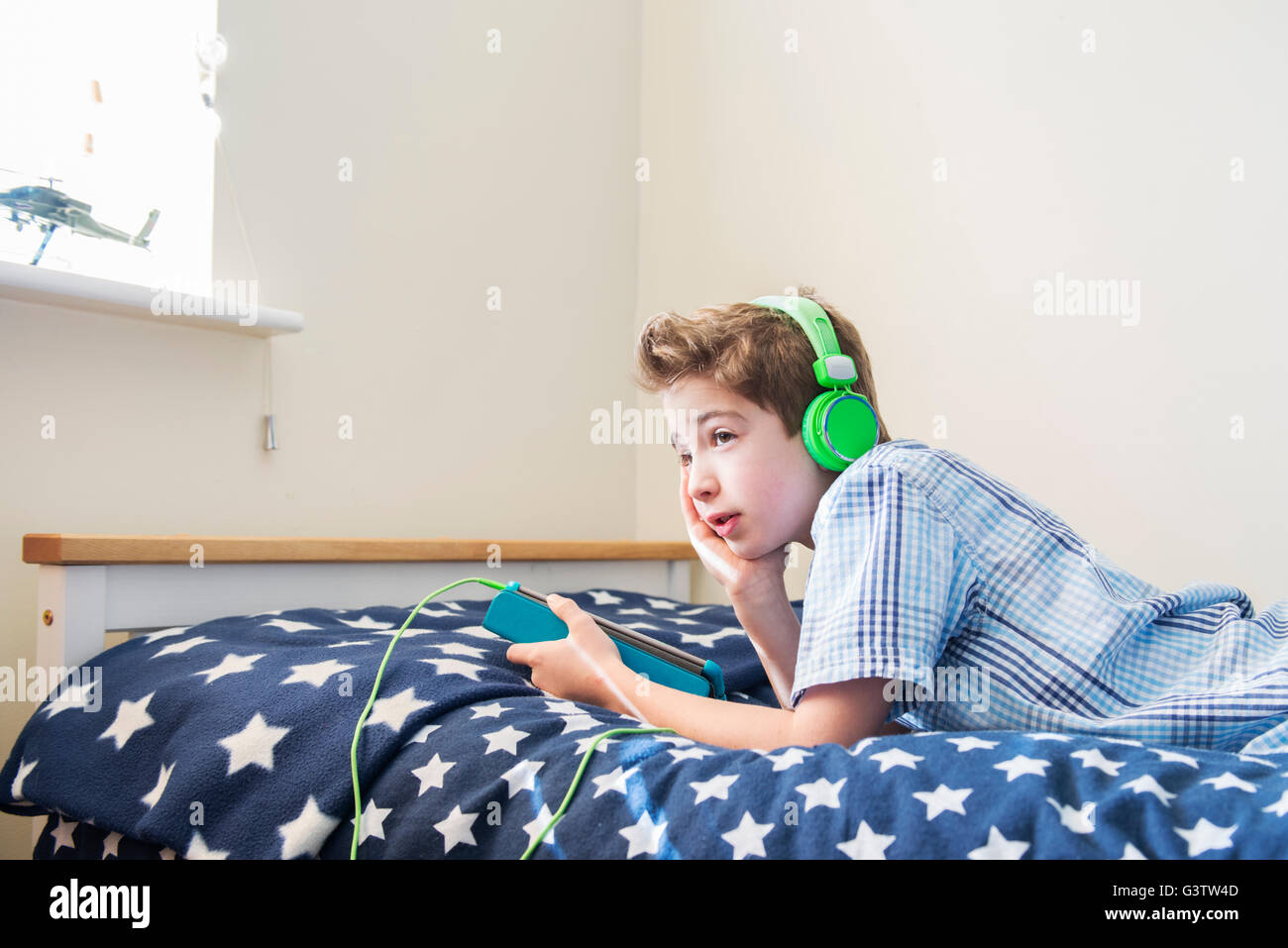 A ten year old boy laying on a bed listening to music on earphones