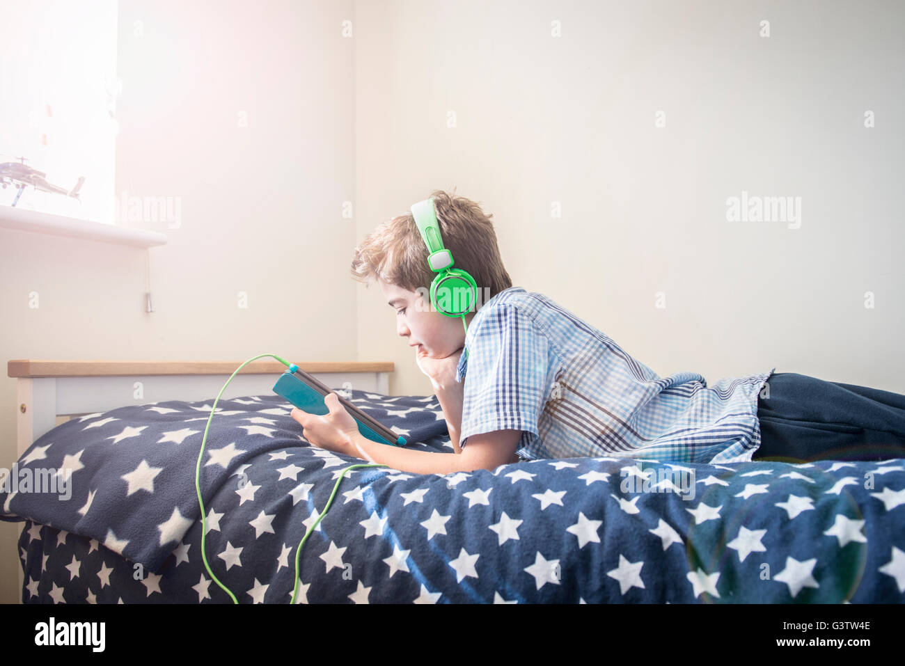 A ten year old boy laying on a bed listening to music on earphones