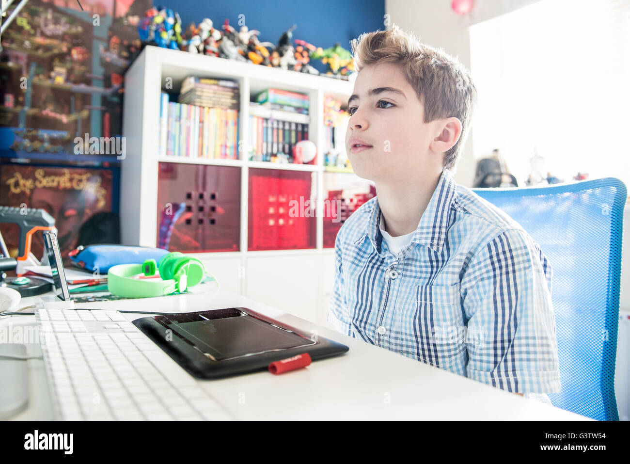 A ten year old boy sitting at a computer in his bedroom. Stock Photo