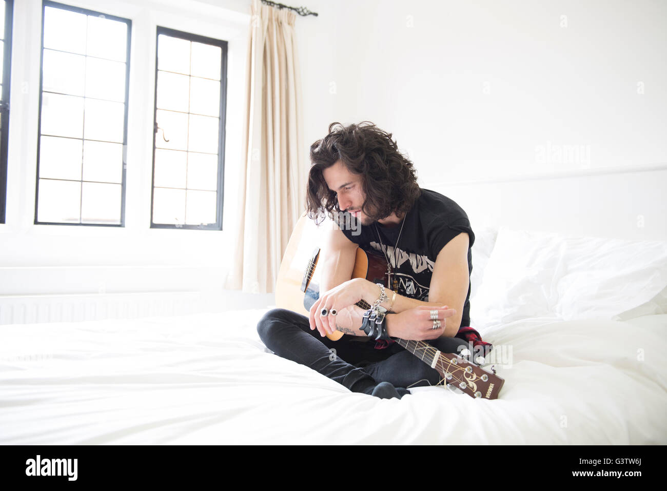 A cool young man sitting on a bed with a guitar. Stock Photo
