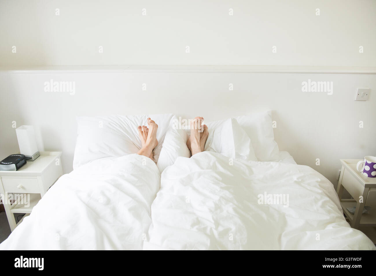 A couple lying in a bed with their feet sticking out from underneath the covers. Stock Photo
