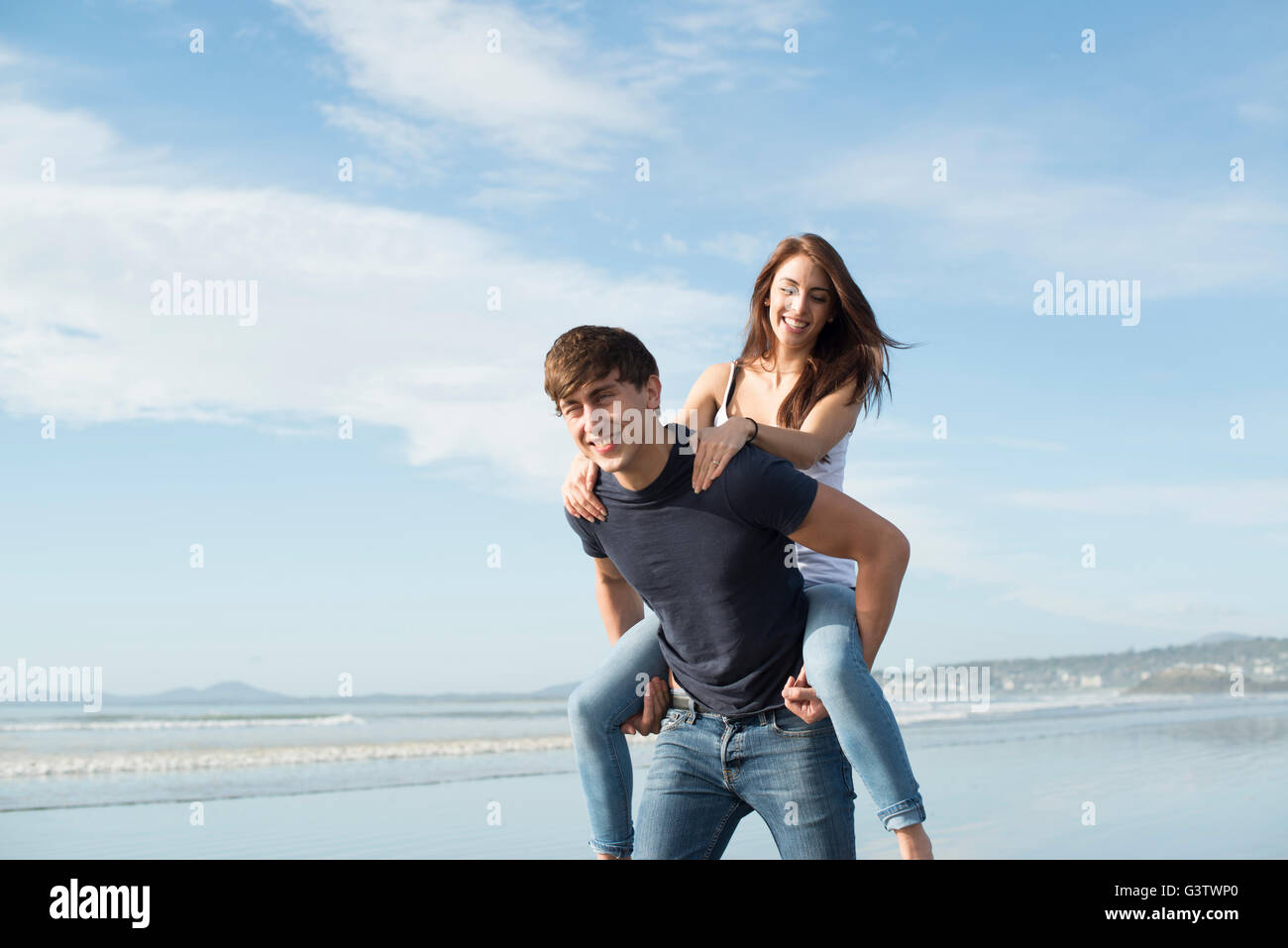 A young couple playing piggy back on the beach at Porthmadog. Stock Photo
