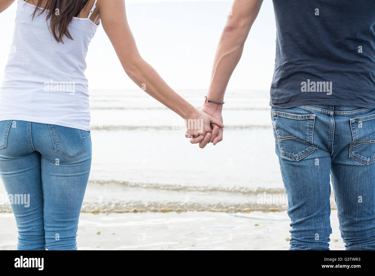 A young couple walk holding hands across the beach at Porthmadog. Stock Photo