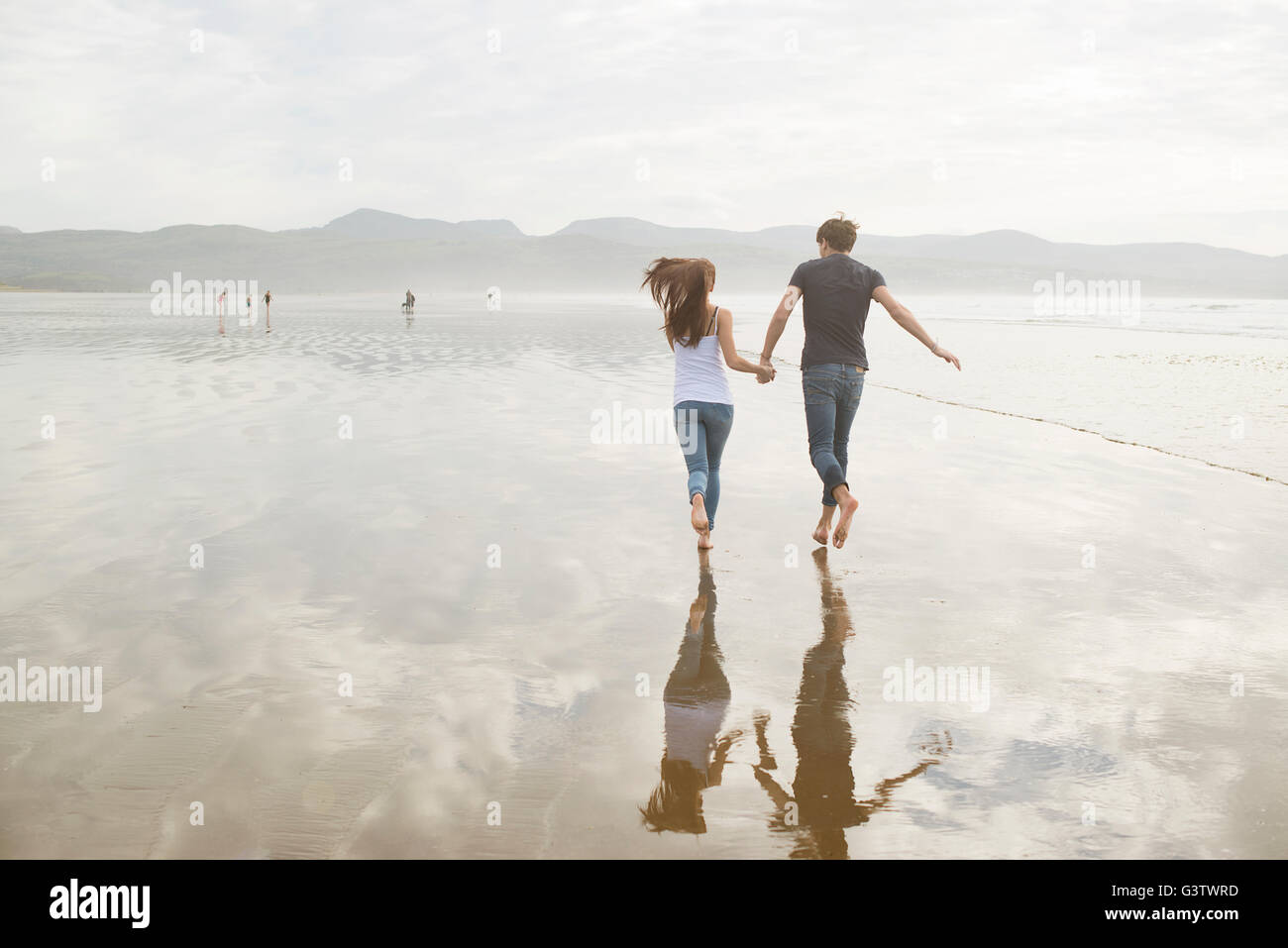 A young couple running whilst holding hands on the beach at Porthmadog. Stock Photo