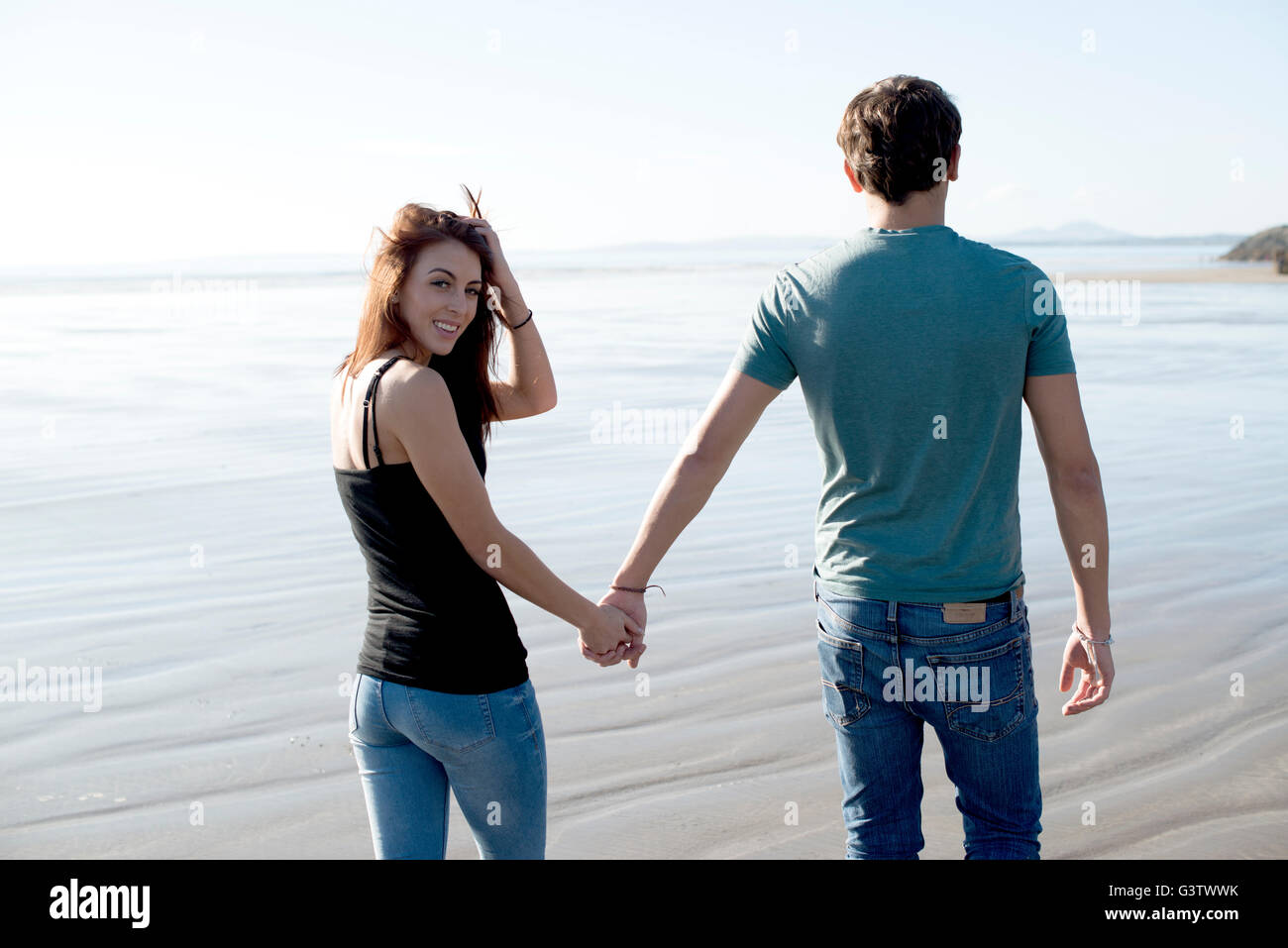 A young couple walk holding hands across the beach at Porthmadog. Stock Photo
