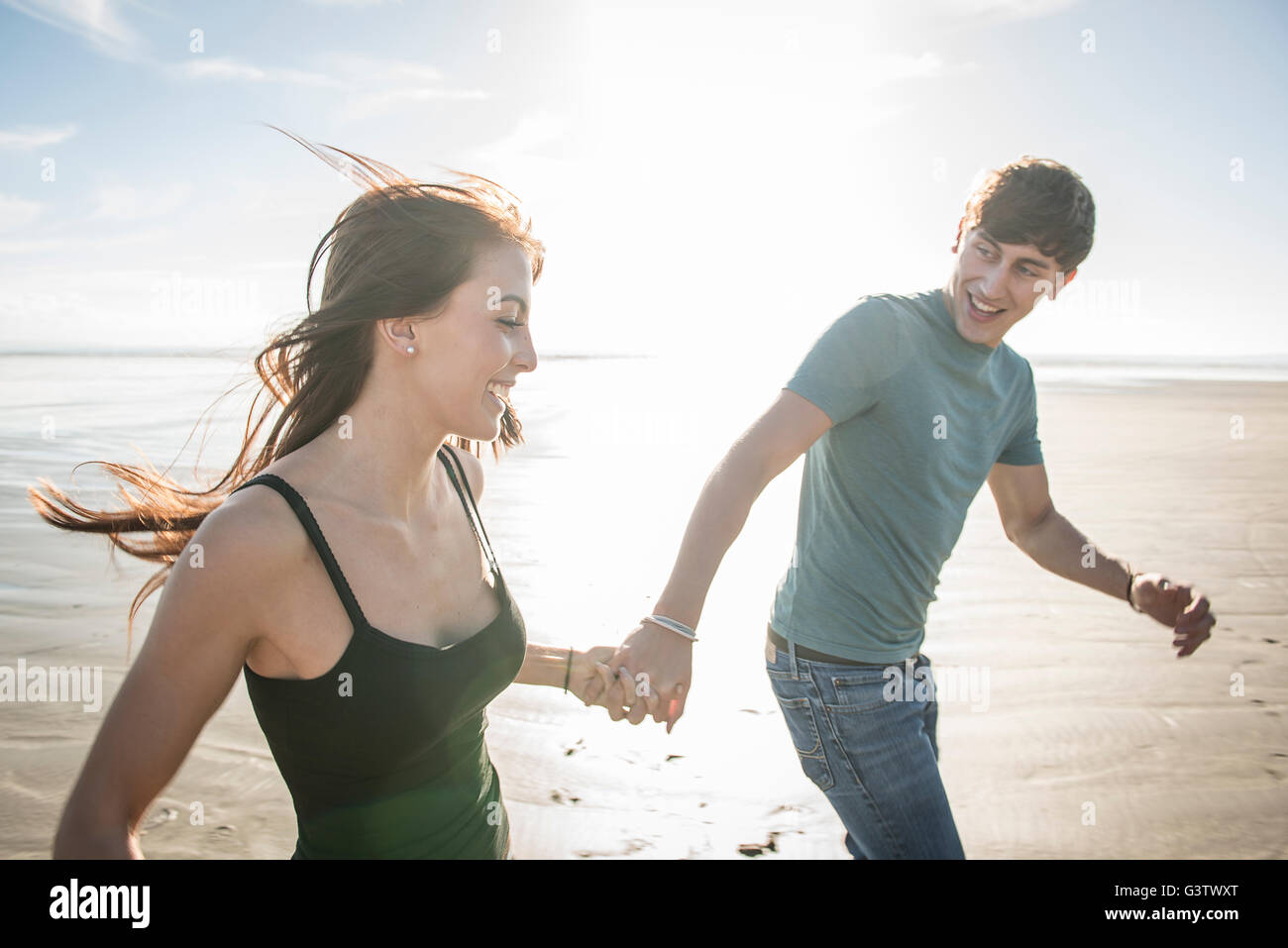 A young couple running whilst holding hands on the beach at Porthmadog. Stock Photo