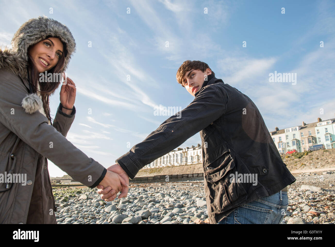 A young couple walking whilst holding hands on the beach at Porthmadog. Stock Photo