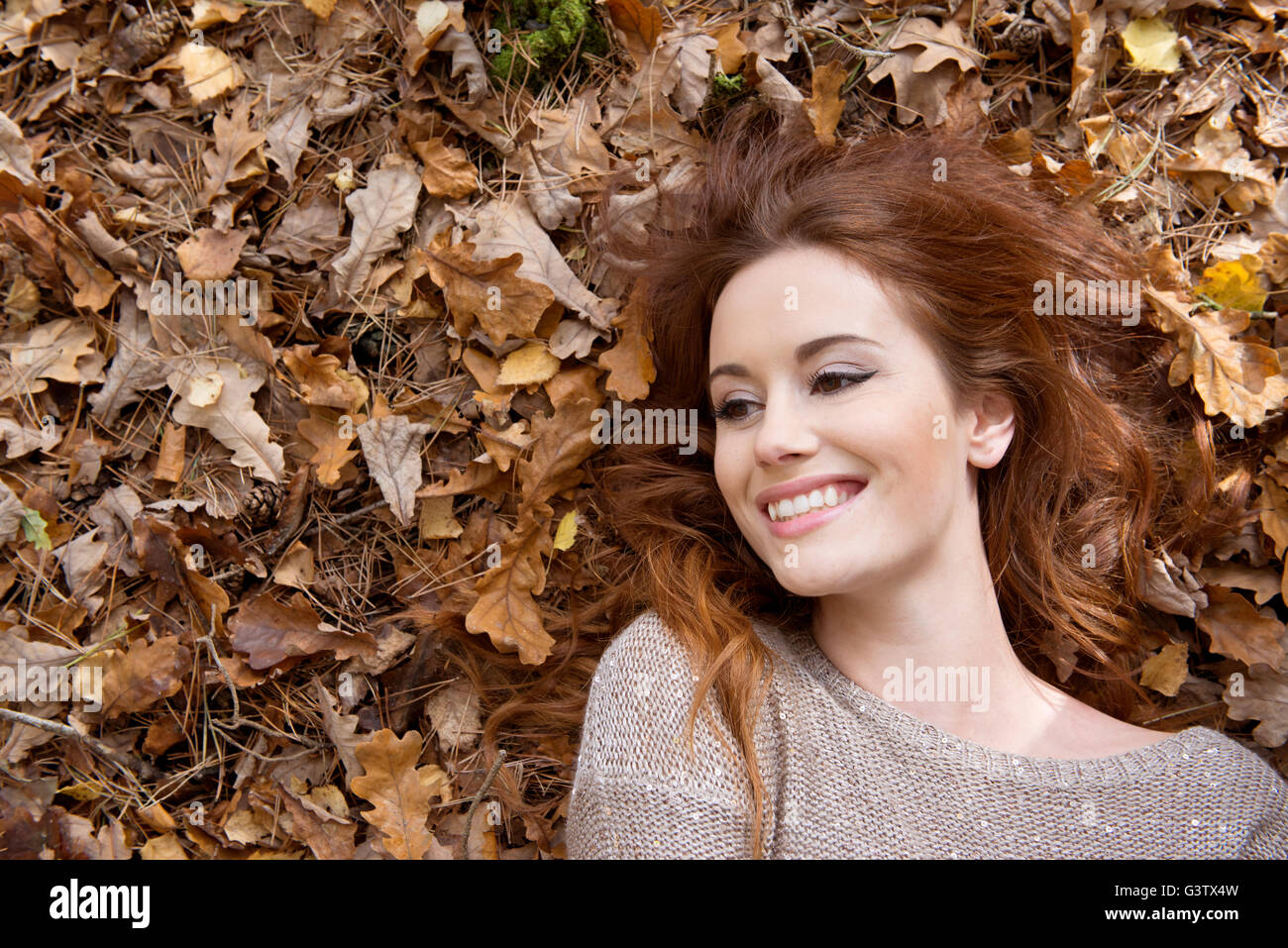 An attractive young woman laying on the forest floor surrounded by leaves. Stock Photo