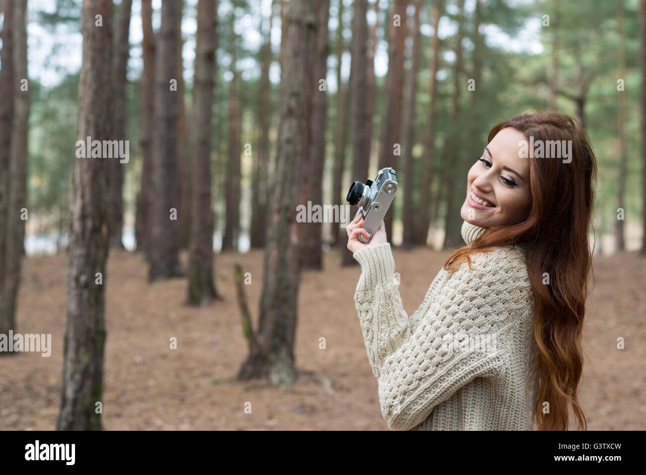 A young woman using a vintage camera in a forest in Autumn. Stock Photo