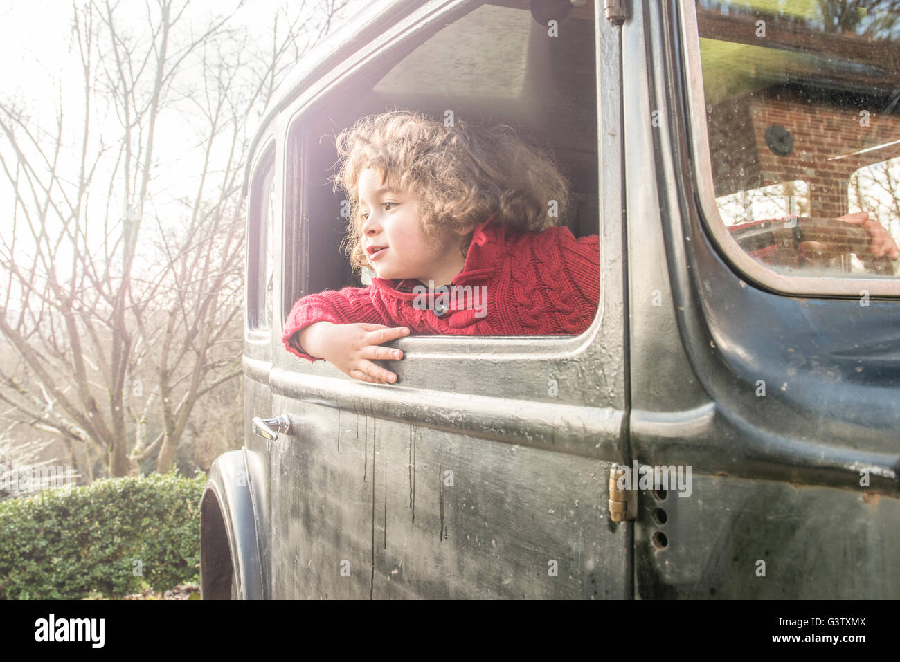 A four year old boy sitting looking out the window of a vintage car. Stock Photo