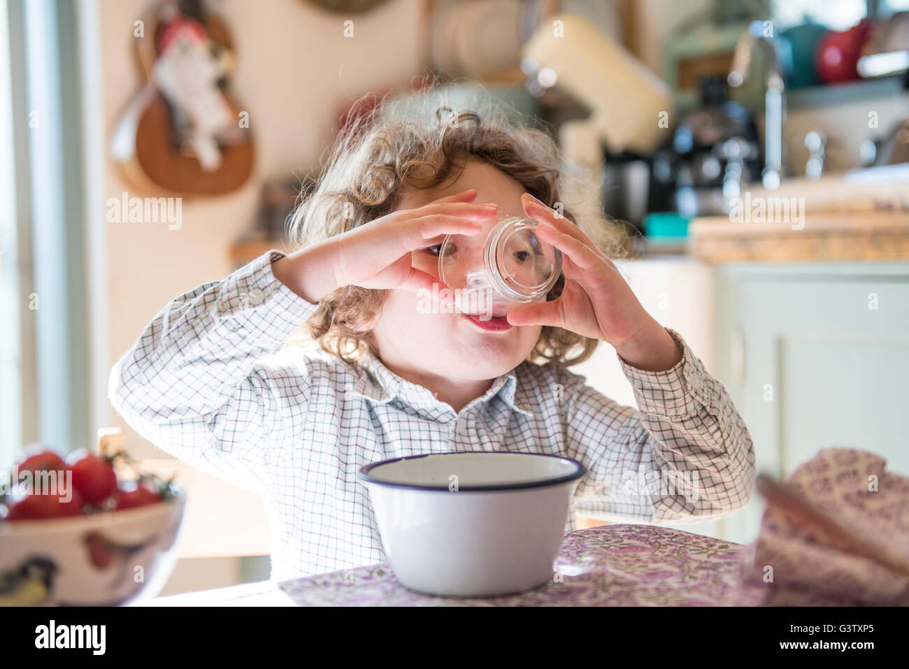 A four year old boy sitting at the kitchen table drinking from a glass. Stock Photo