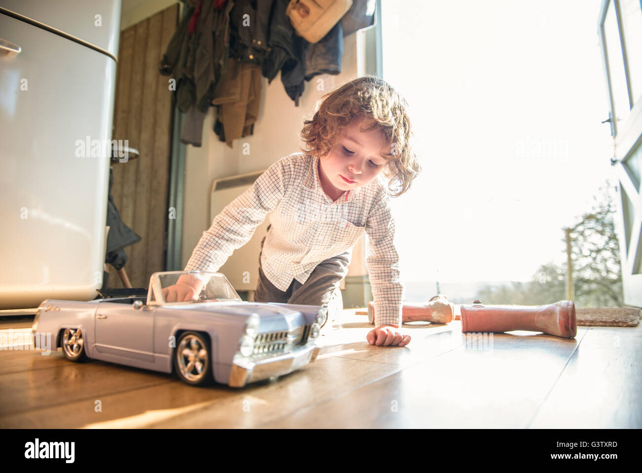 A four year old boy sitting at a back door playing with a toy car. Stock Photo