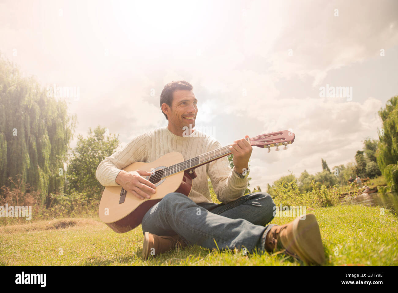 A man playing a guitar by the banks of the River Cam in Cambridge. Stock Photo