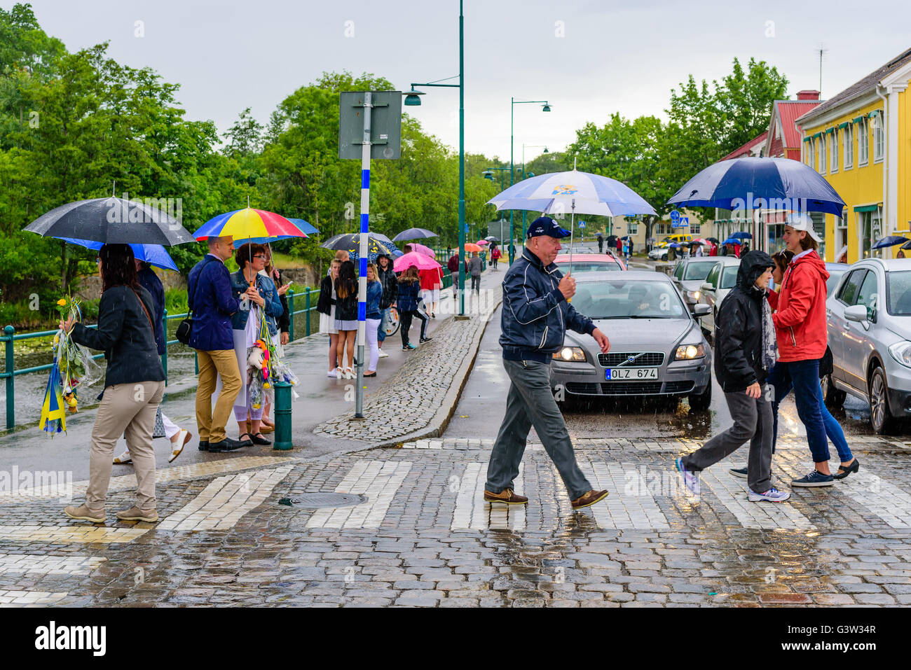 Ronneby, Sweden - June 10, 2016: People walking across a street in town in the middle of a rainfall. Traffic has stopped and Stock Photo