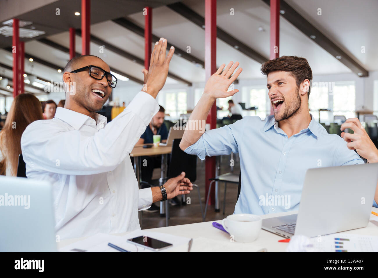 Two cheerful excited young men giving high five and working in office ...