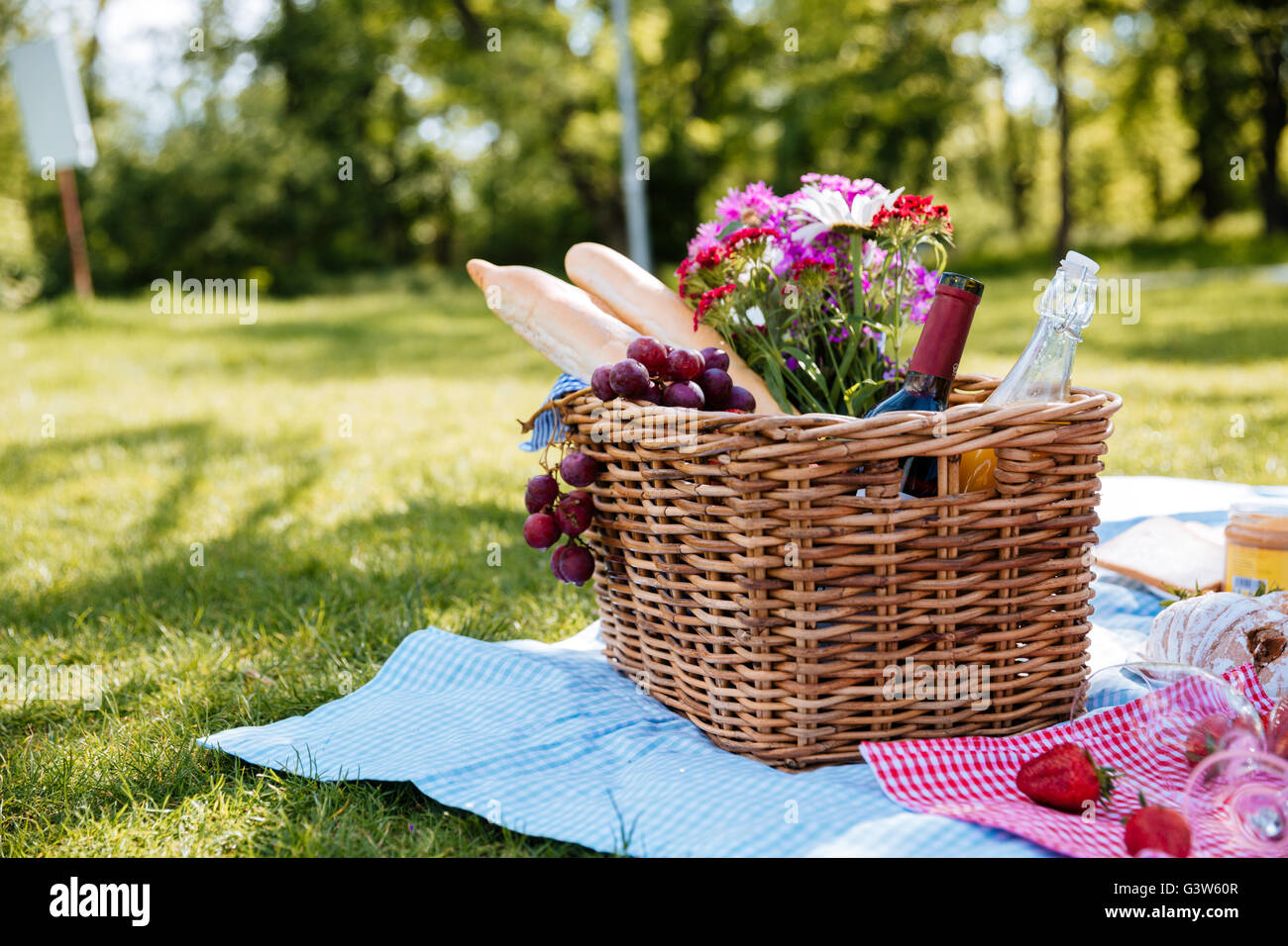 Closeup of picnic basket with drinks, food and flowers on the grass Stock Photo