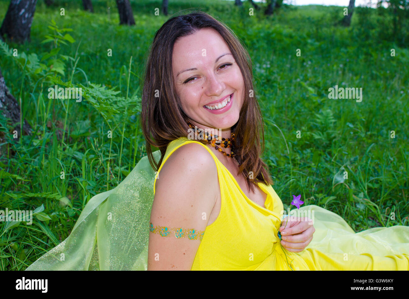 The girl sits in the wood on a green grass and smiles, the girl, green ...