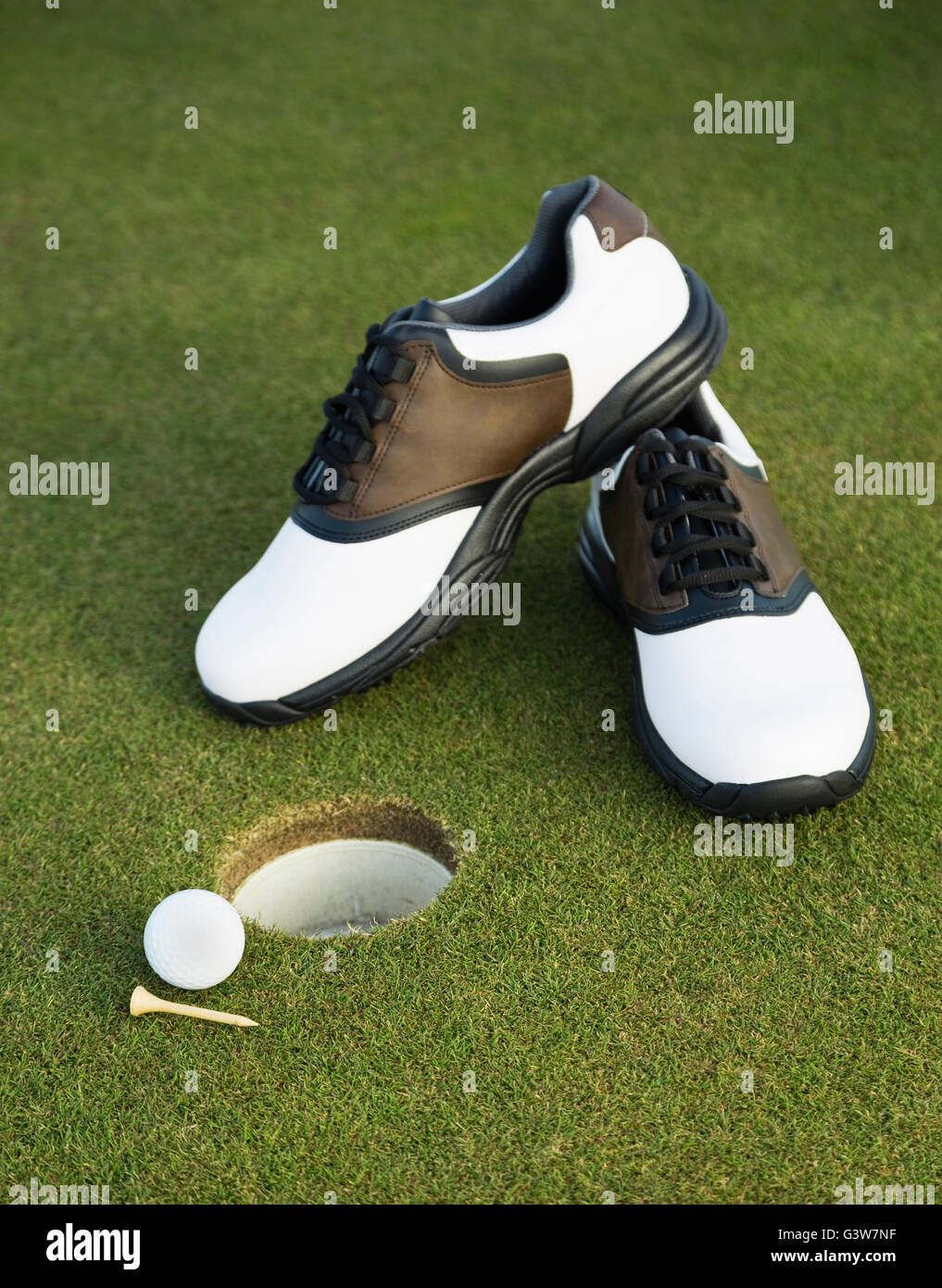 Golf shoes, ball and tee on golf course by hole Stock Photo