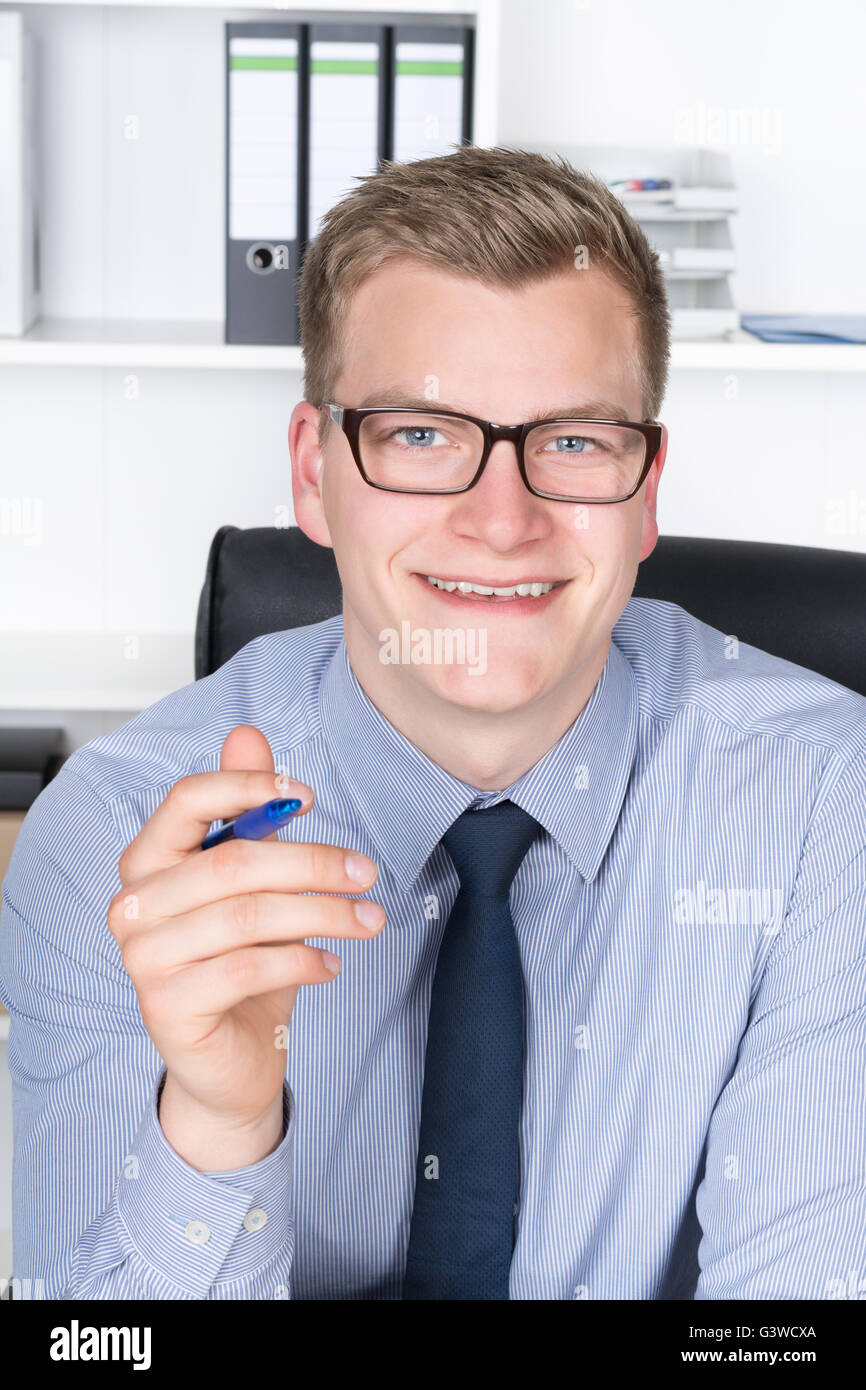 Young smiling businessman with glasses is holding a pen in his hand ...