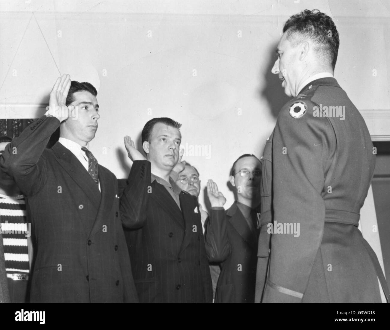 Joe DiMaggio, left, former home run king and outfielder of the NY Yankees, is sworn into the US Army with other inductees by Capt M.A. Branson, right, at an induction center on the West Coast. Joe's induction shrinks his income from a baseball salary of $50,000 a year to the $50 a month as a buck private. Stock Photo