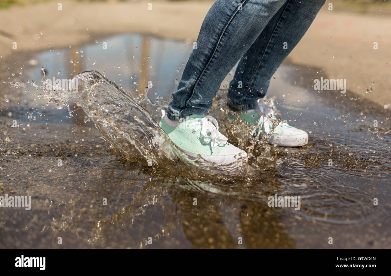 Woman in gumshoes jumping in a puddle. Close up shot of foots in a shoes with water splashes Stock Photo