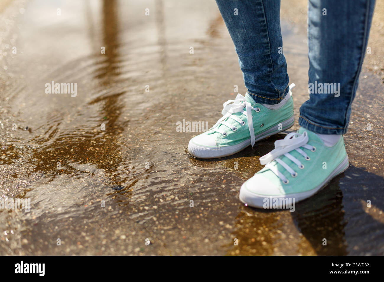 Woman in sport shoes standing in a puddle. Close up shot of foots in a water Stock Photo