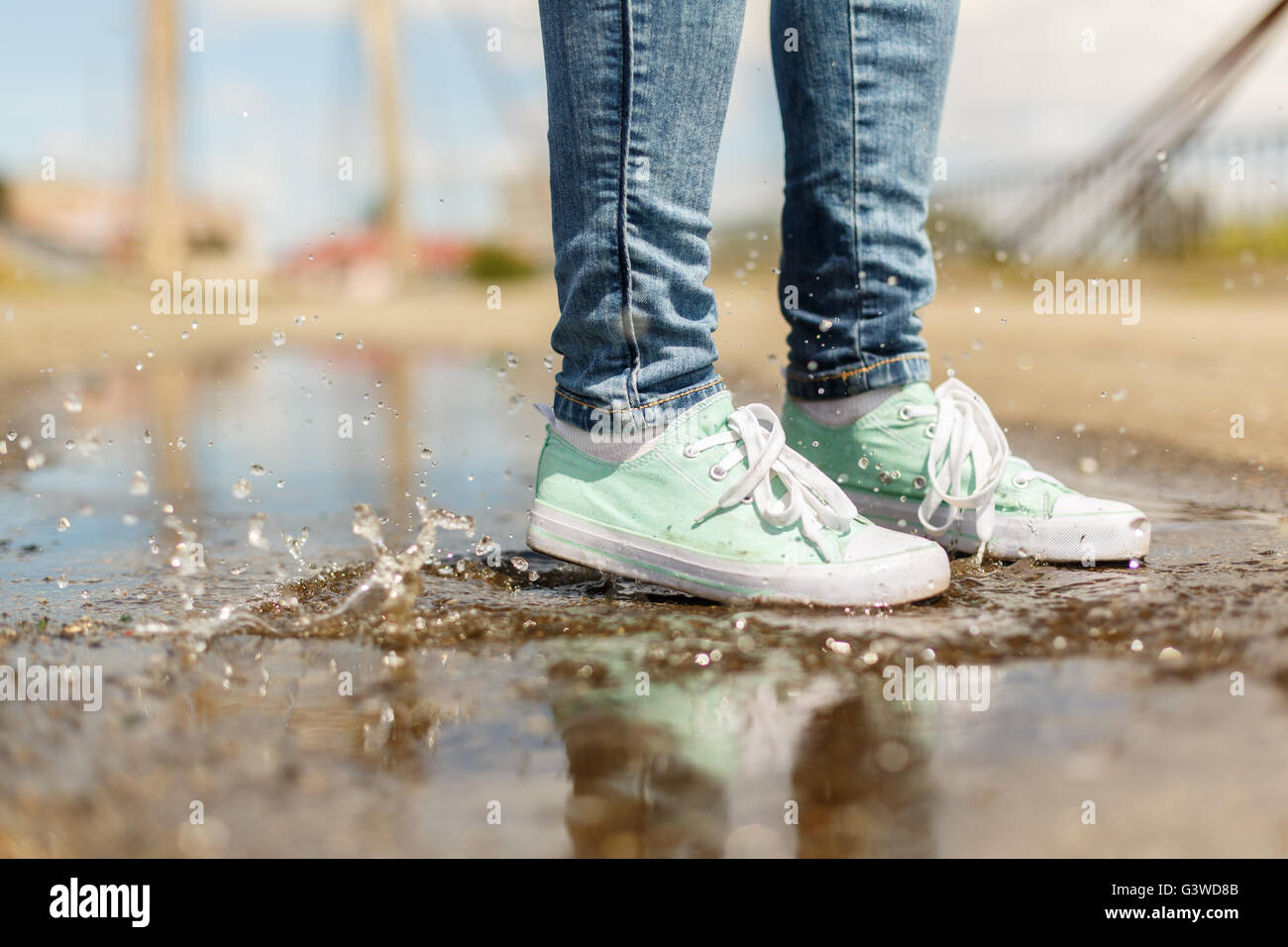 Woman in gumshoes jumping in a puddle. Close up shot of foots in a shoes with water splashes Stock Photo