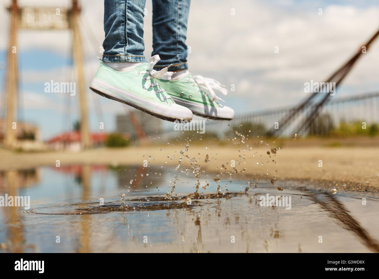 Foots of a woman in a sport shoes flying over a puddle during jumping. Close up shot of foots over the water Stock Photo