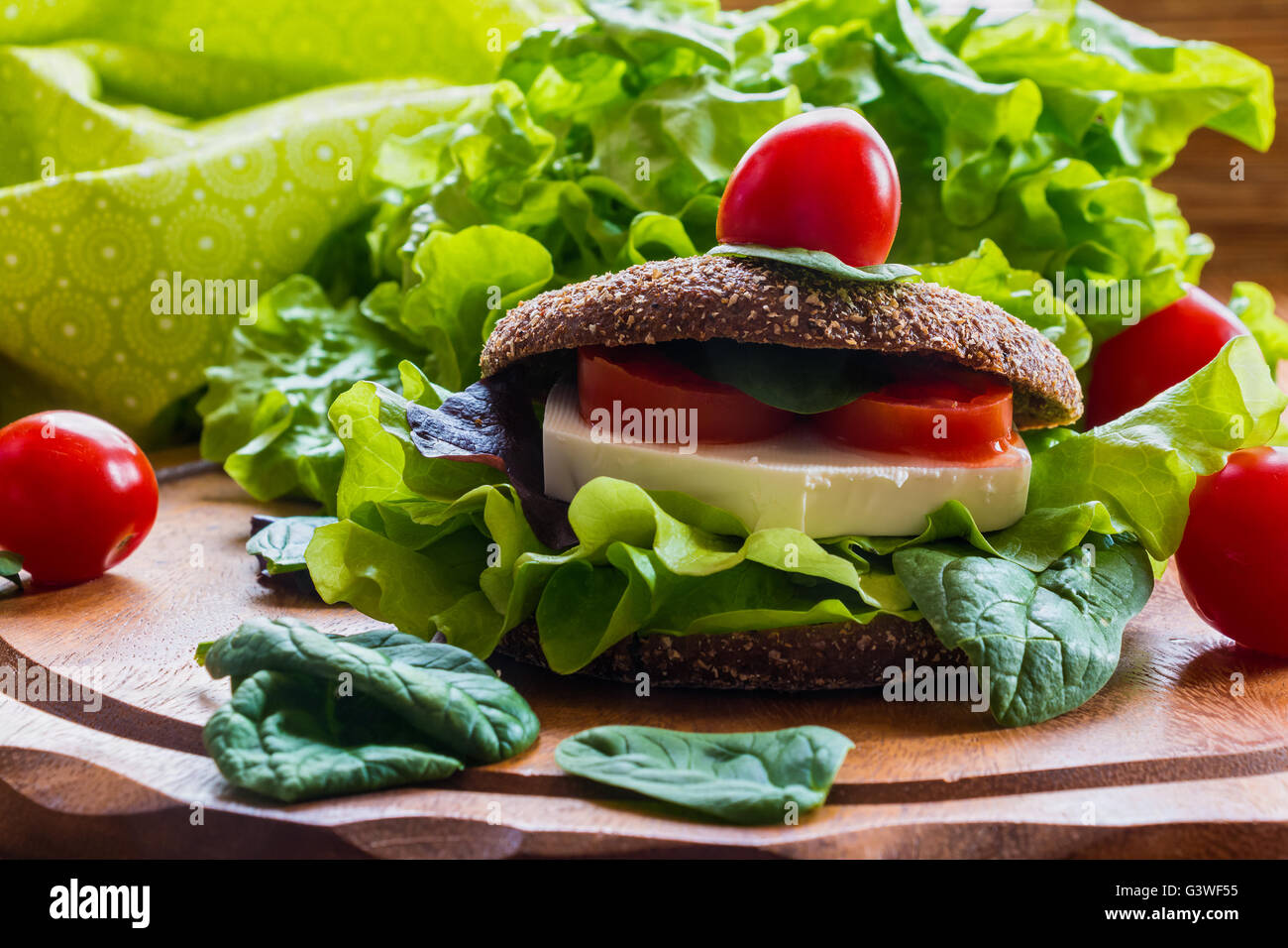 Burger: vegan burger with lettuce, fresh cherry tomatoes and feta cheese on wooden background. Stock Photo