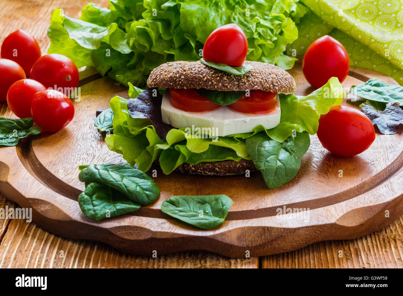 Burger: vegan burger with lettuce, fresh cherry tomatoes and feta cheese on wooden background. Stock Photo