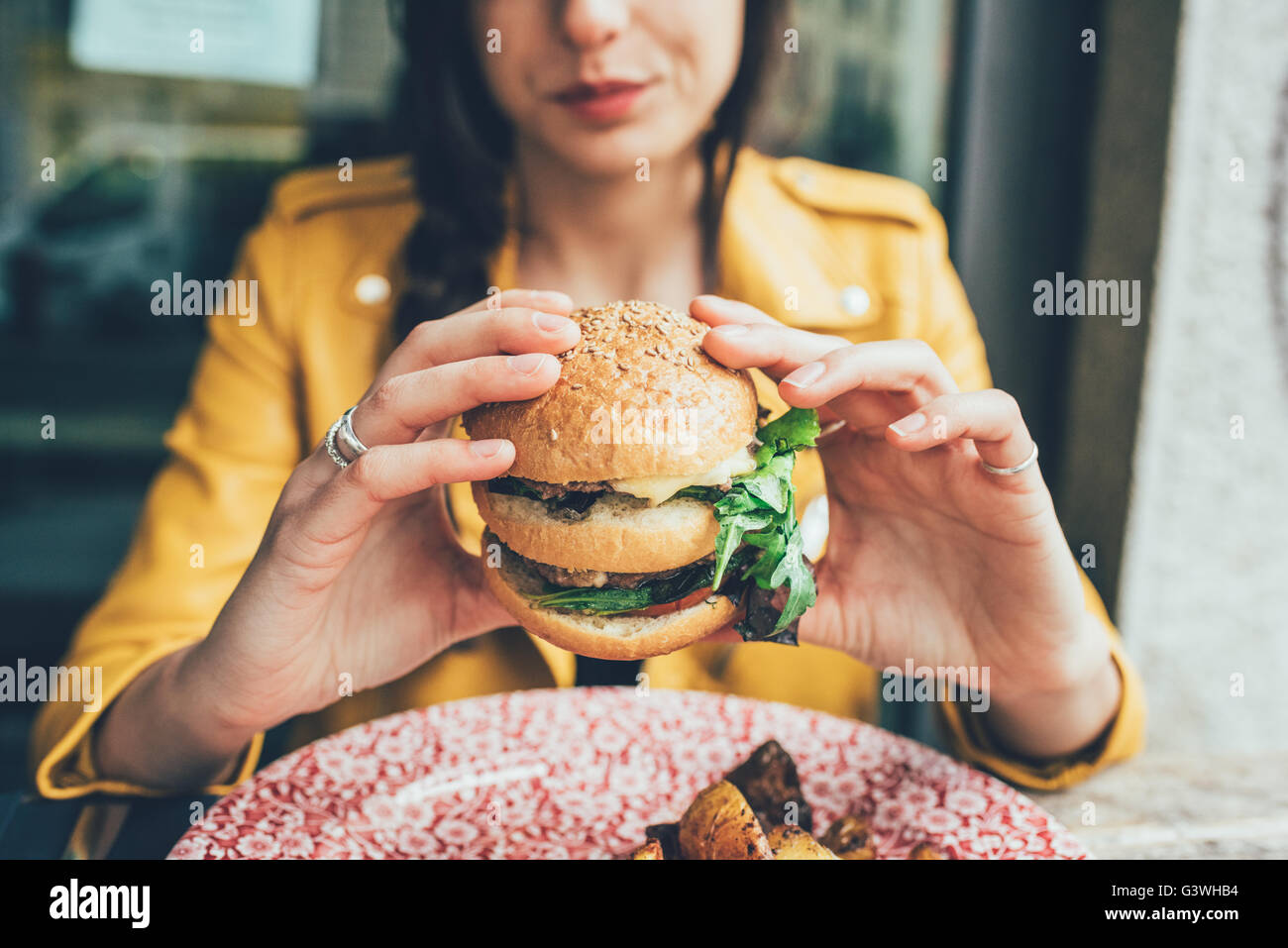 Close up on the hands of a young woman sitting holding an hamburger - hunger, food, meal concept Stock Photo