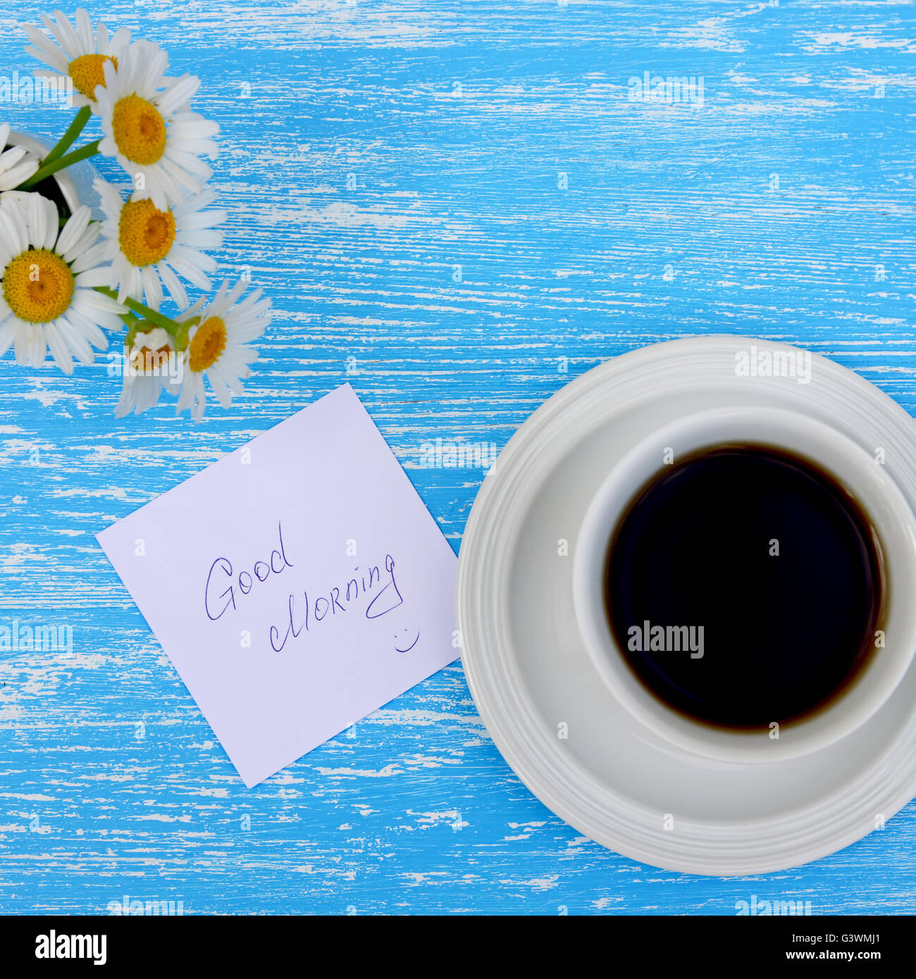 Daisy flowers and cup of tea with good morning note on rustic blue