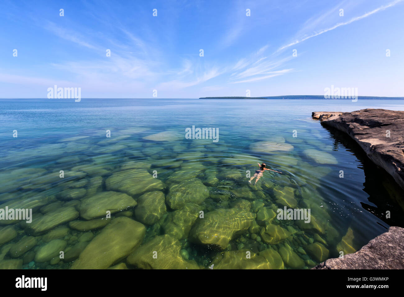 A girl swims in Lake Superior in the upper peninsula of Lake Michigan. Rocks are visible through the glass like, pristine waters Stock Photo